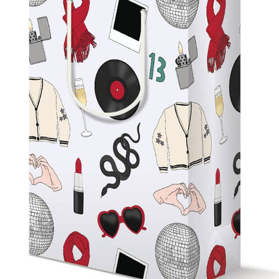 white gift bag with Taylor Swift themed drawings relating back to all of her iconic albums or songs: heart shaped sunglasses, lighter, cardigan, red lipstick, black snake, red scarf