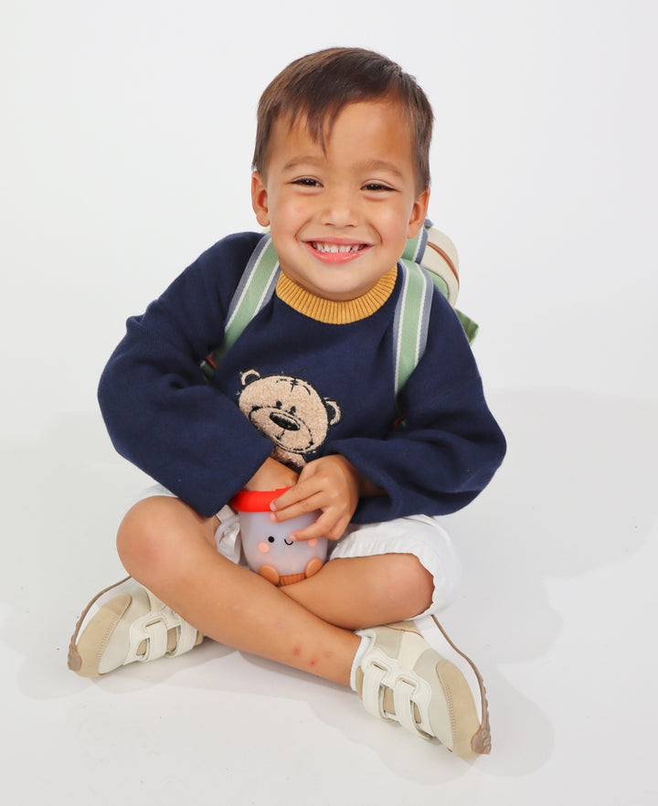 Child wearing a navy sweater with a bear design, holding a mushroom snack cup, on a white background