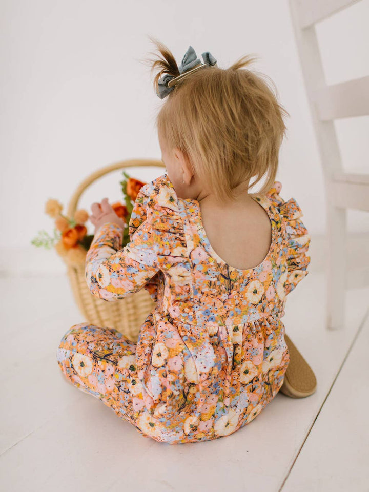 Child in a floral outfit sitting on a white floor with a basket of flowers in the background