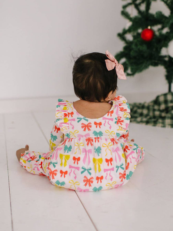 Child wearing a colorful bow-patterned outfit sitting on a couch with a Christmas tree in the background.