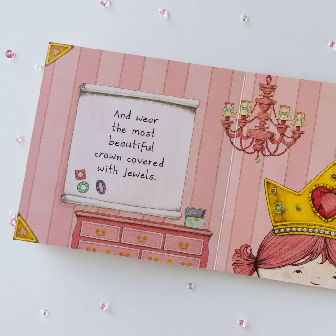 Illustrated book with a princess theme, including a crown and jewelry on a pink background.