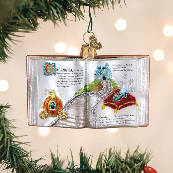 Decorative Christmas ornament shaped like an open book with Cinderella-themed illustrations, hanging on a tree.