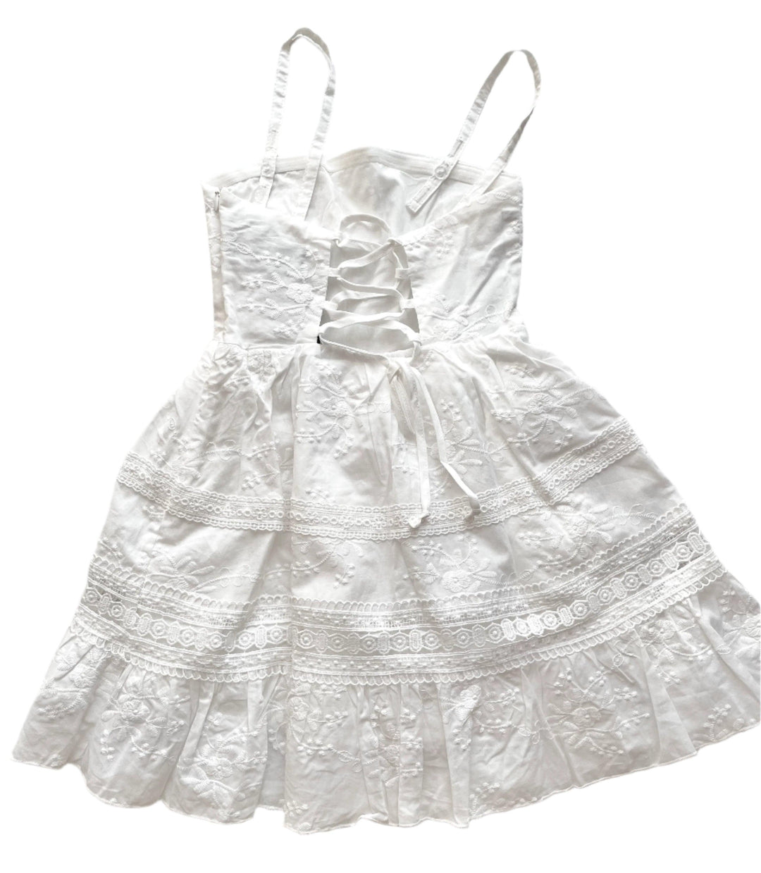 white spaghetti strap dress with stripes of lace along skirt and white embroidery all over the bodice. the dress laces up the back. 
