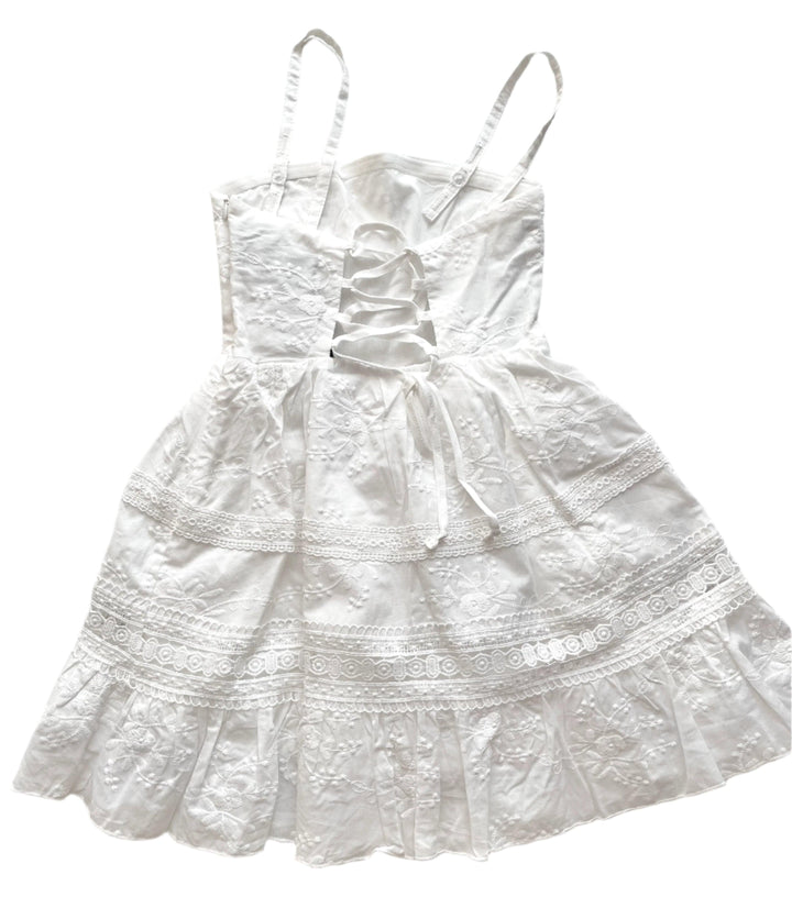 white spaghetti strap dress with stripes of lace along skirt and white embroidery all over the bodice. the dress laces up the back. 