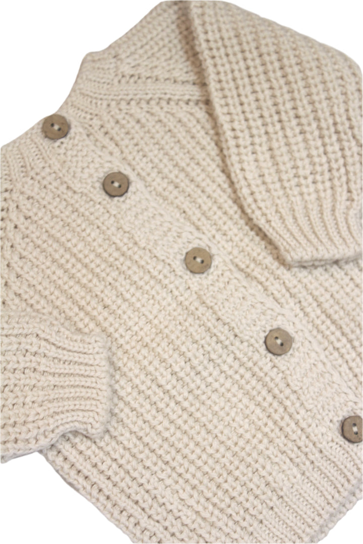 knit baby sweater in creme color with buttons going down the center of the sweater. 