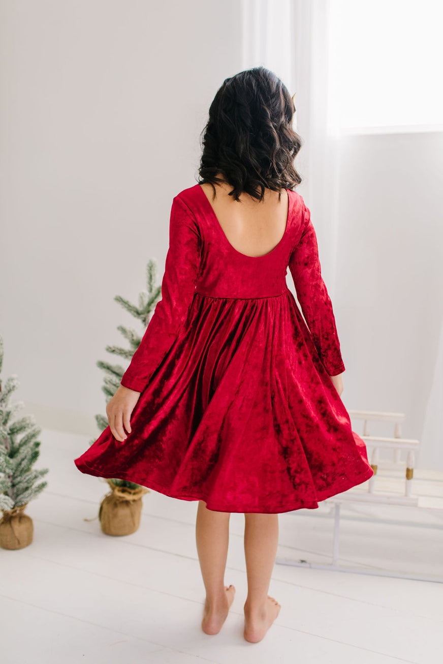 oack of child wearing a red dress with long sleeves in a minimalistic room.