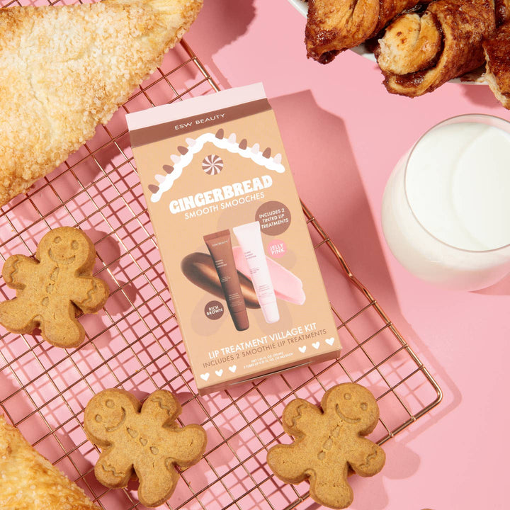 Gingerbread-themed skincare kit on a pink surface with cookies and a mug.