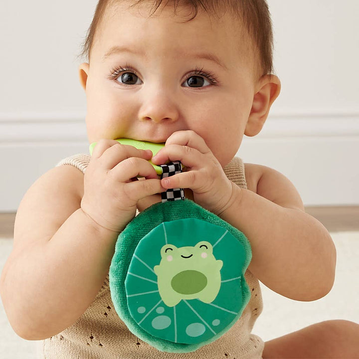 Baby holding a green teething toy with a frog design.