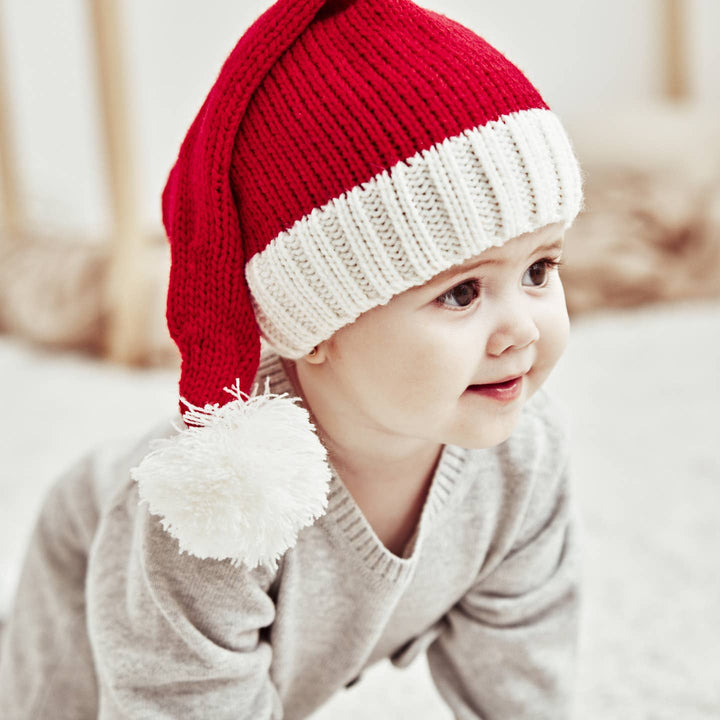 Child wearing a red and white knit hat with a fluffy pom-pom on a blurred background