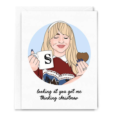 greeting card with Sabrina Carpenter on the front holding a cookie and mug making a face like she is enjoying what she is eating. Has a Christmas message and depiction