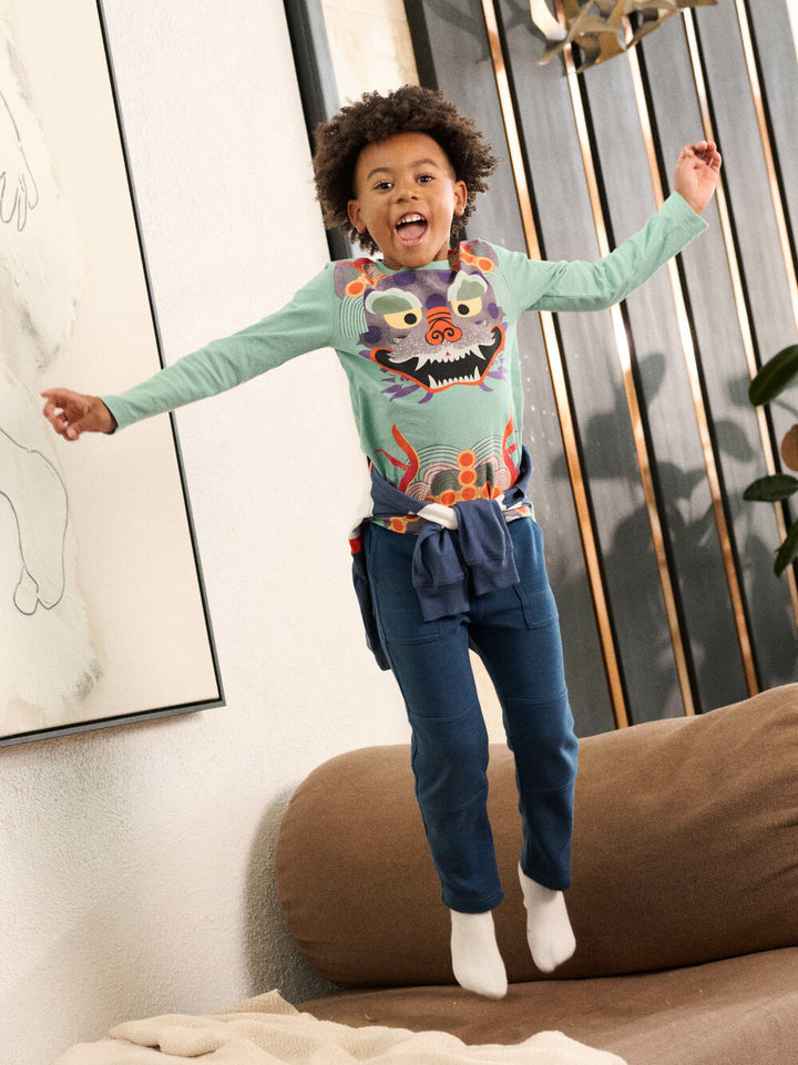 Child wearing a colorful sweater with a tiger design, jumping on a couch.