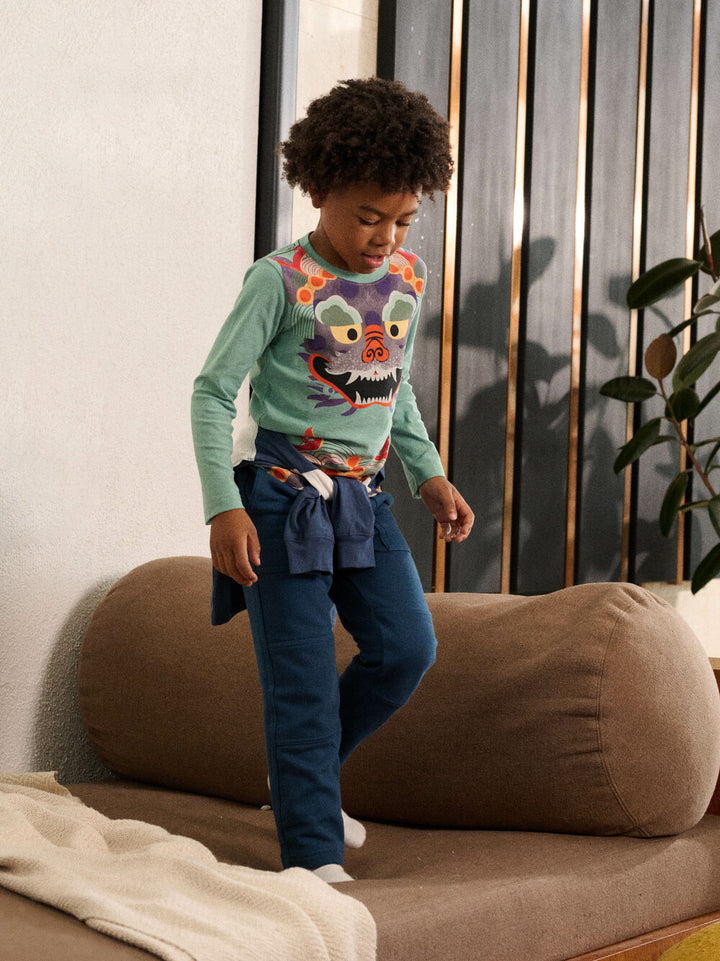 Child wearing a colorful sweater with a cartoon character, standing on a couch.