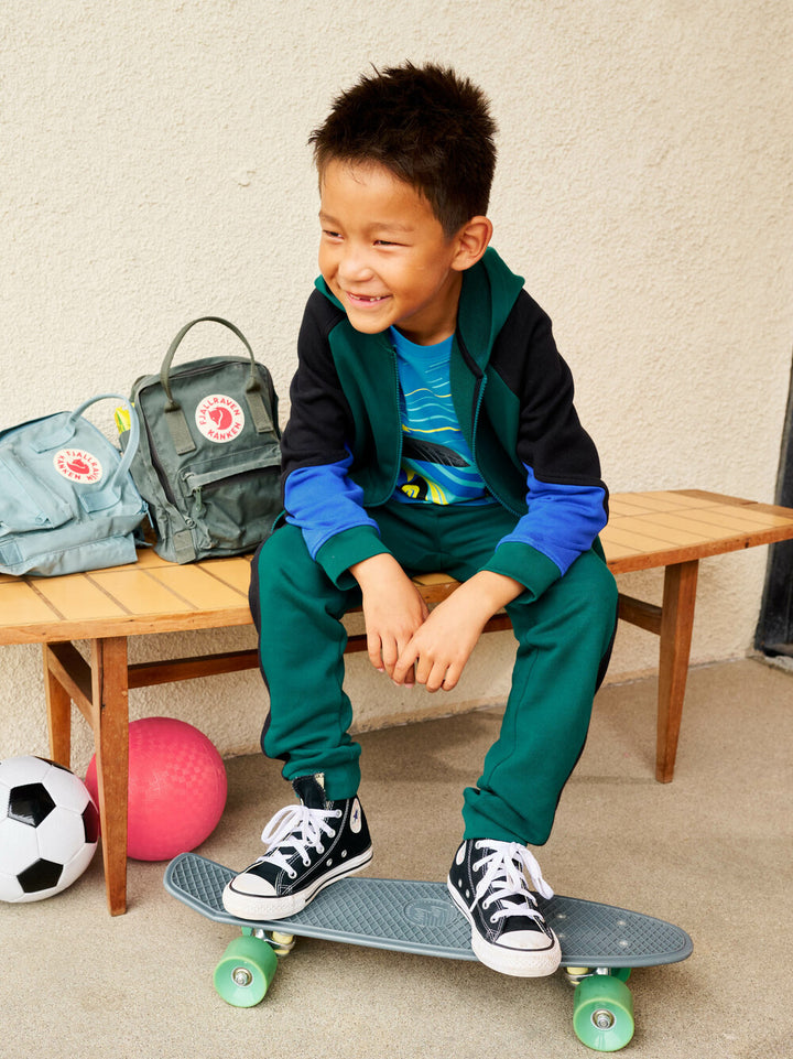 Child sitting on a skateboard with sports equipment in the background