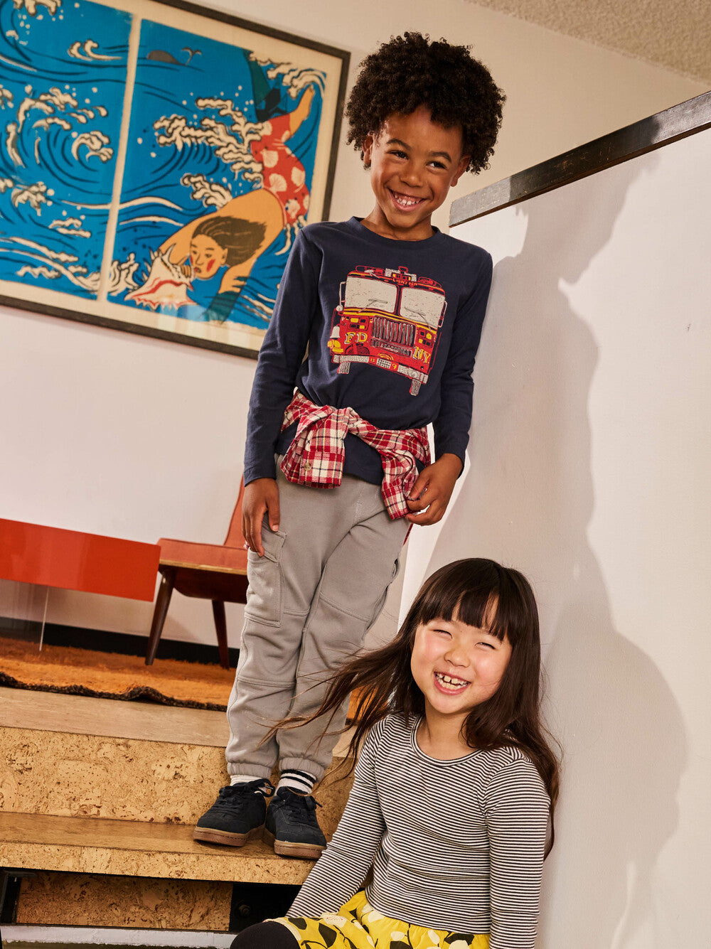 Two children standing on a staircase with a colorful painting in the background