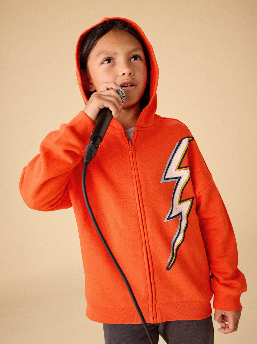 young boy wearing a bright red hooded sweatshirt with ivory lightning bolt on the hood and front of the sweatshirt. 
