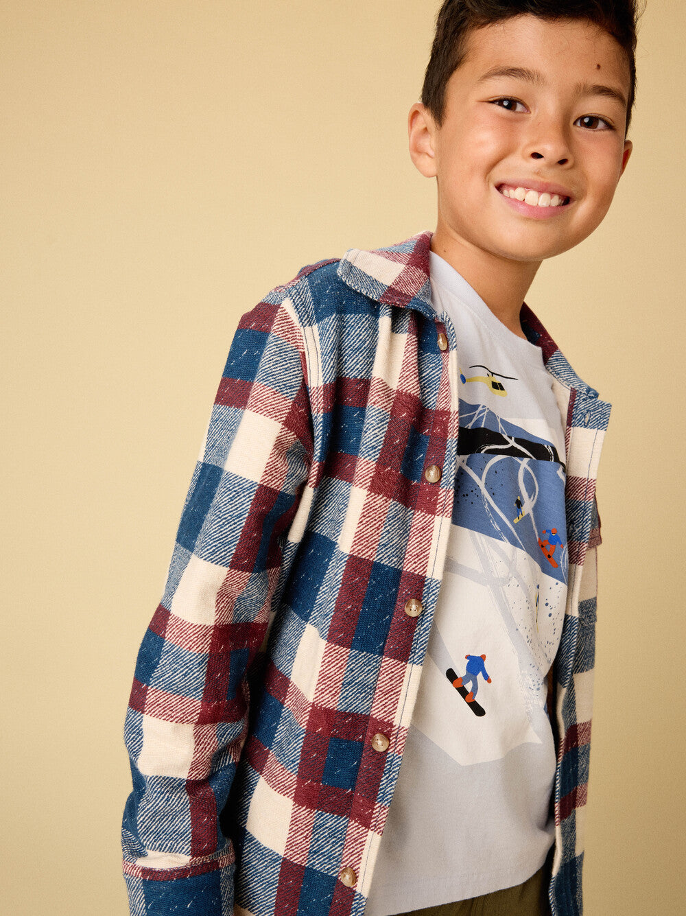 Child wearing a plaid shirt over a graphic t-shirt on a beige background
