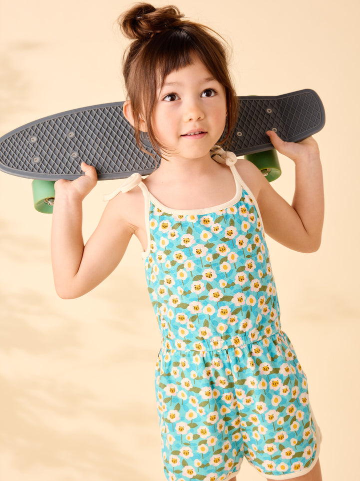 Child wearing a floral romper holding a skateboard against a beige background