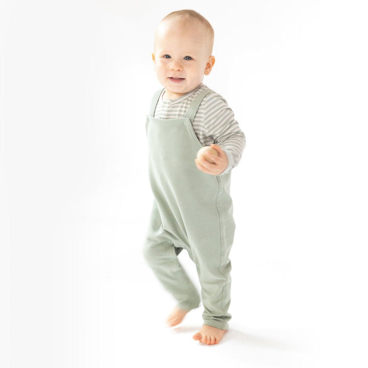 baby modeling french terry overalls in sage green. 