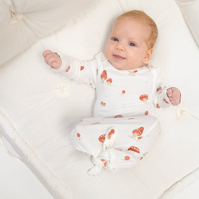 baby dressed in baby onesie that has mushrooms all over it with happy faces on them