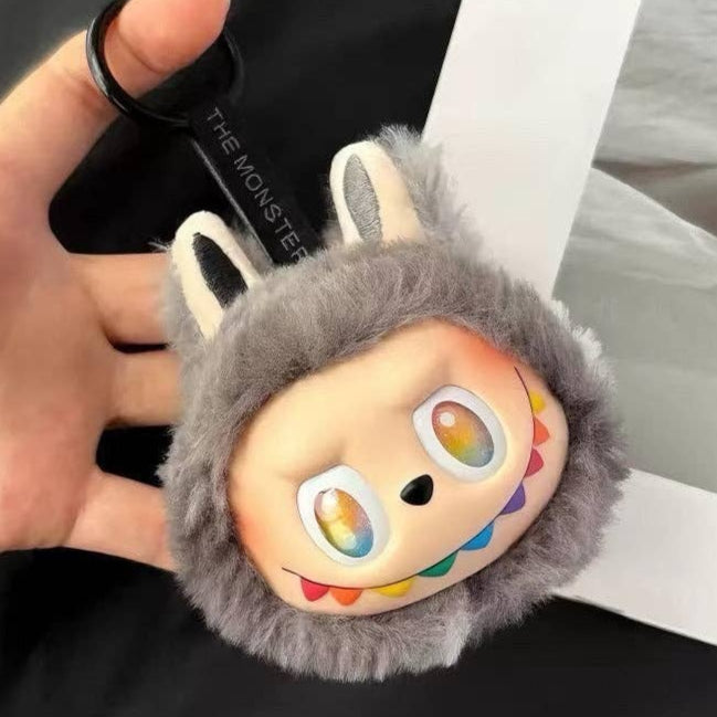 Plush keychain with cartoon face and rainbow eyes held by a hand.