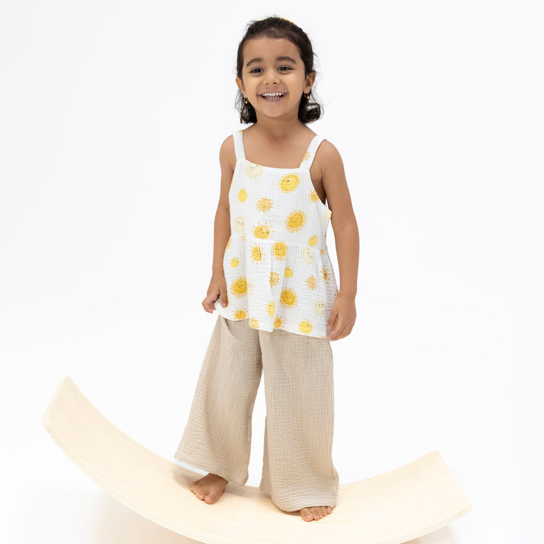 Young girl wearing a white sleeveless top with yellow floral patterns and beige pants on a white background