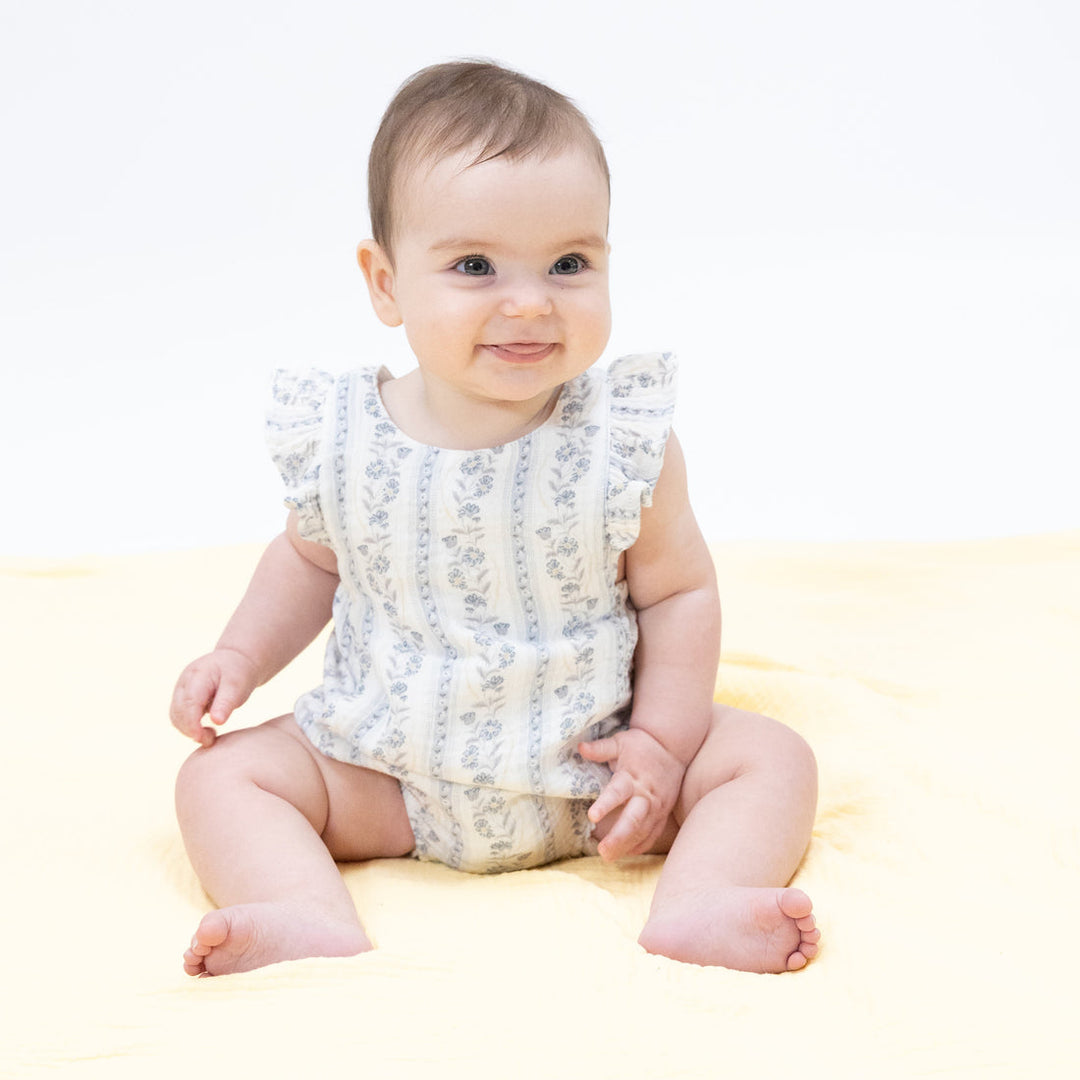 Baby sitting on a light-colored surface wearing a floral romper.