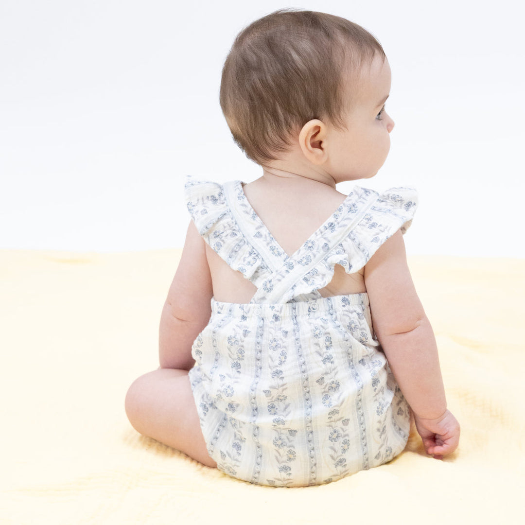 Baby wearing a floral romper sitting on a light-colored surface