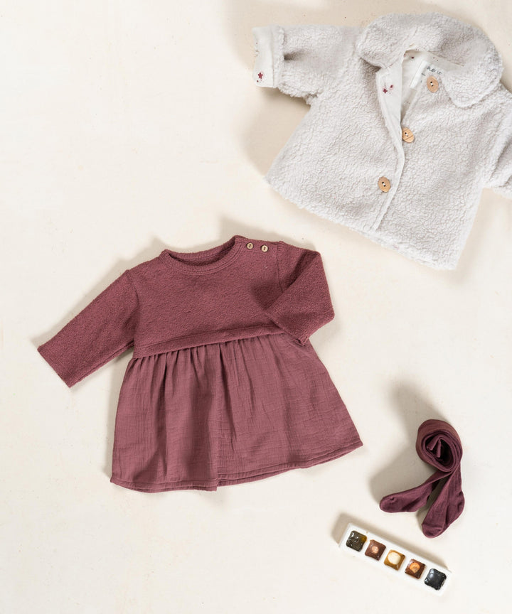 Children's clothing including a maroon dress, beige sherpa jacket, and burgundy tights on a light beige background.