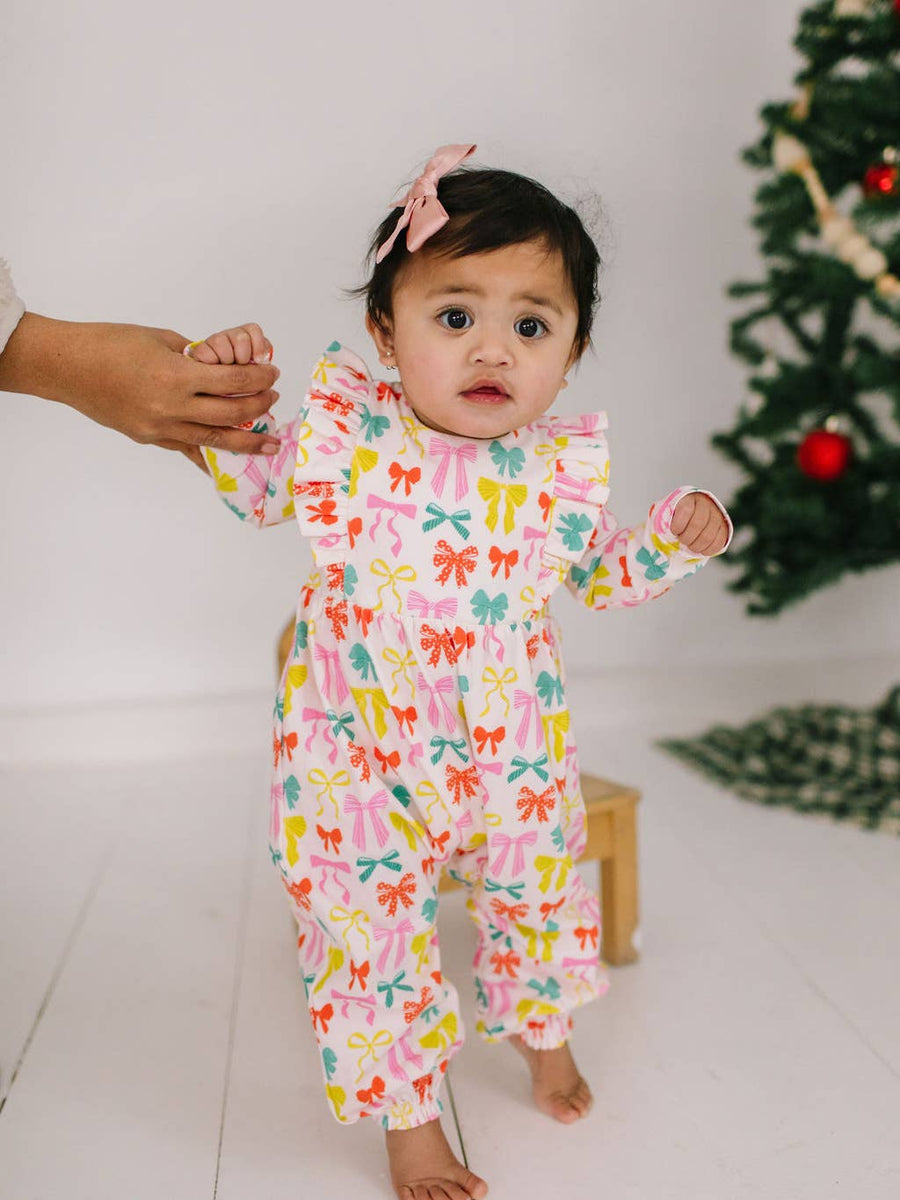 Baby in a colorful outfit with a Christmas tree in the background