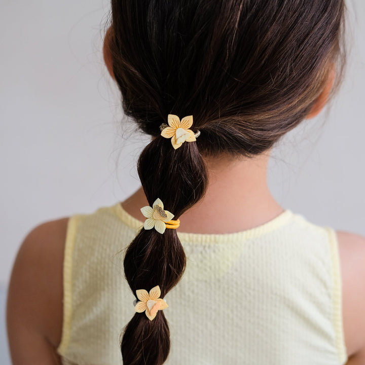 Girl with braided hair adorned with floral hair ties against a plain background