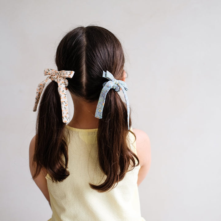 Person with long hair tied in pigtails using decorative ribbons against a plain background