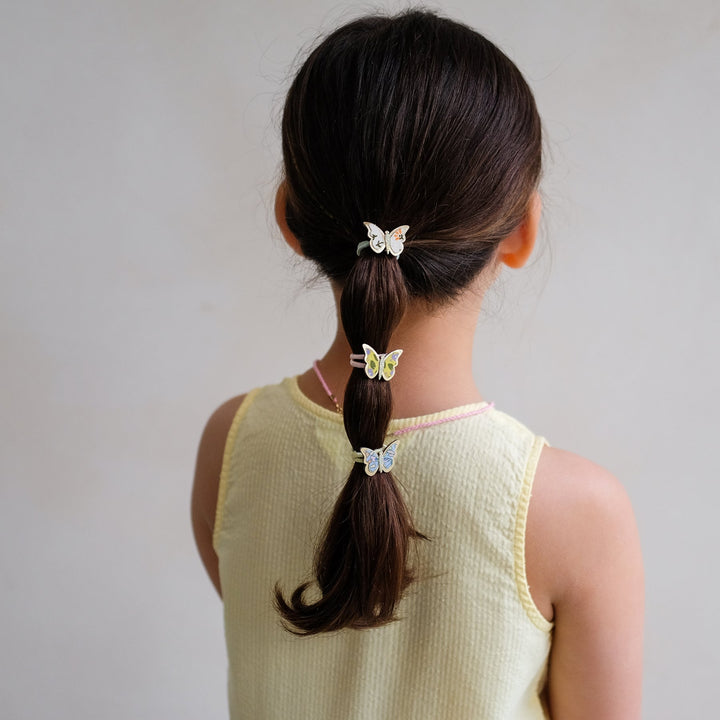 Person with a ponytail wearing butterfly hair clips on a plain background