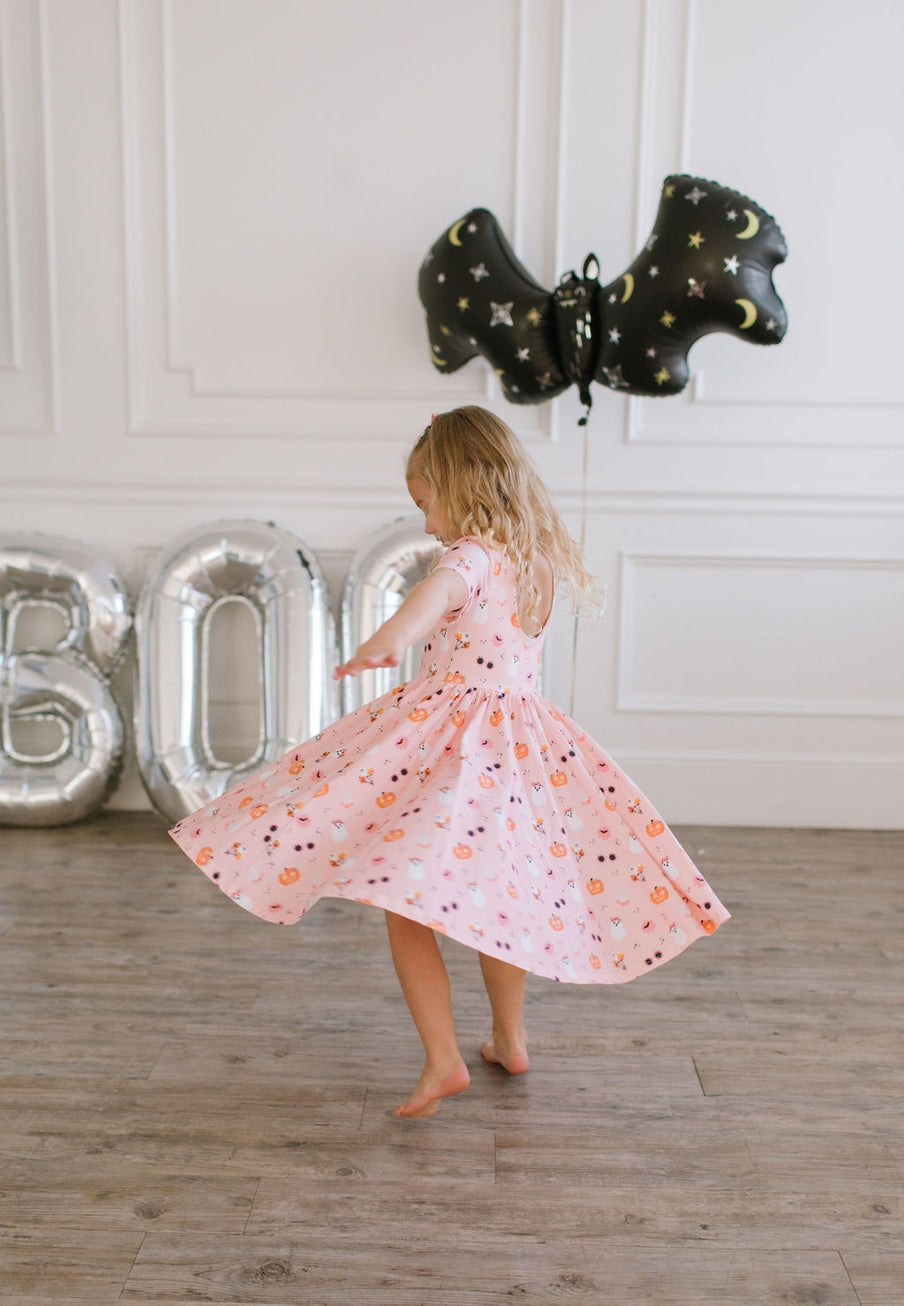 Child in a pink dress standing in front of large metallic letters spelling 'BOY' with black balloon stars above.