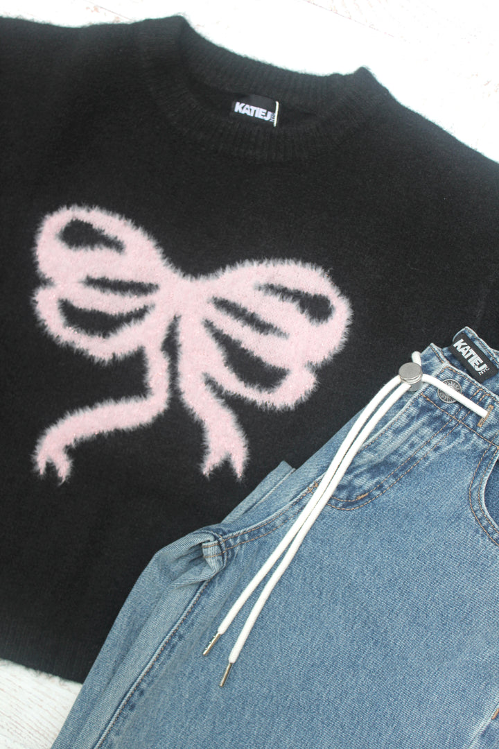 Black sweater with a white bow design and blue jeans on a light gray background