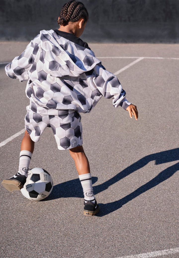 Person playing soccer on a paved surface wearing a patterned outfit.