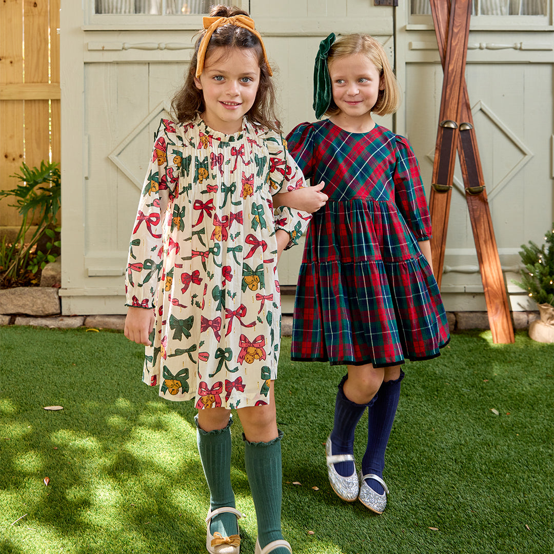 Two young girls in dresses standing on grass with a wooden structure in the background