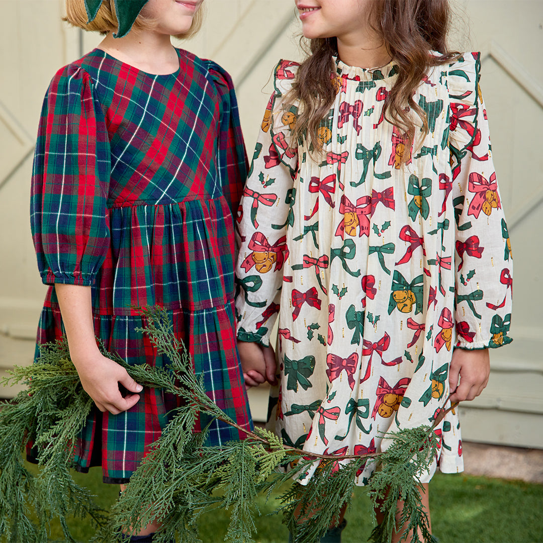 Two children wearing festive dresses holding greenery.
