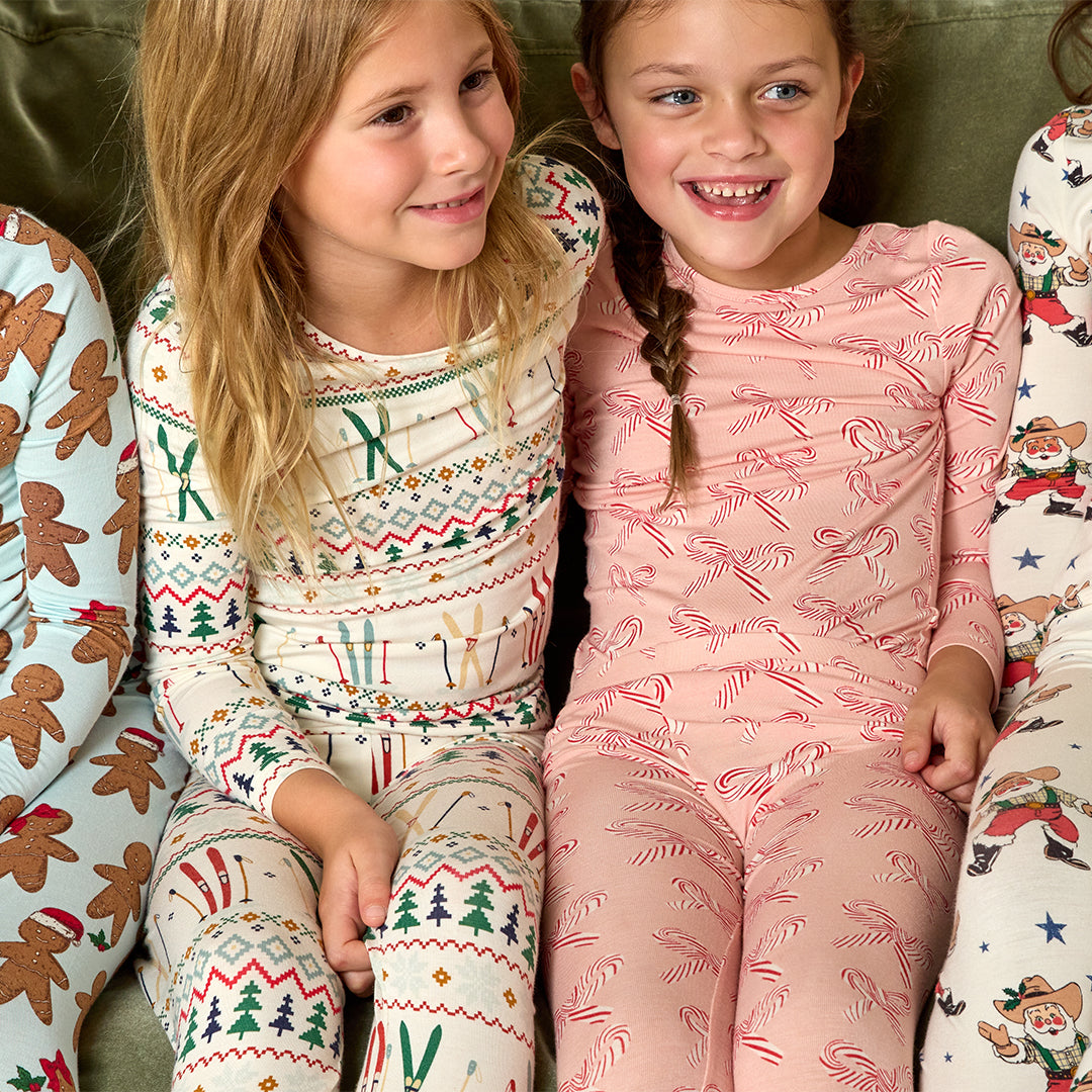 Two children wearing patterned pajamas sitting together on a couch.
