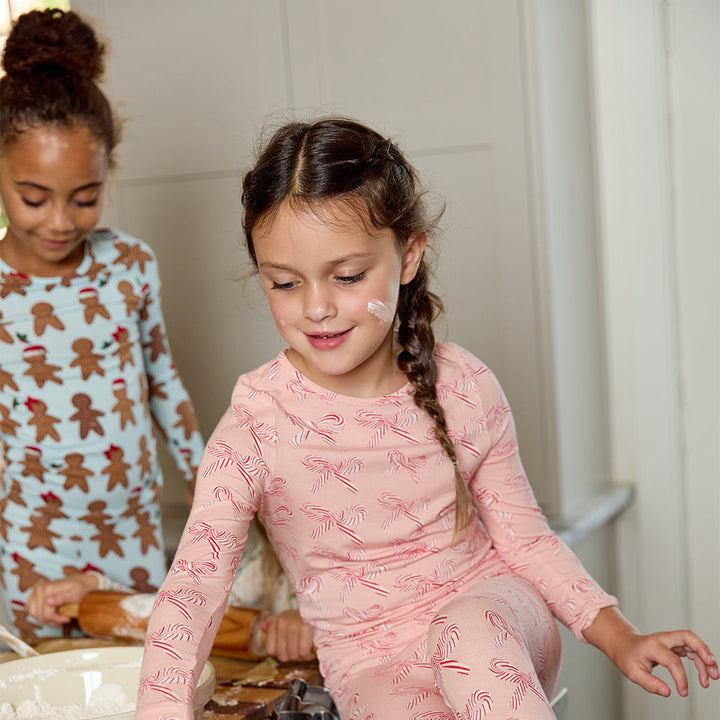 Two young girls in pajamas with gingerbread men designs in a kitchen.