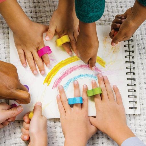 This picture shows children drawing with heart shaped crayons. wearing them on their fingers and making marks on paper. 