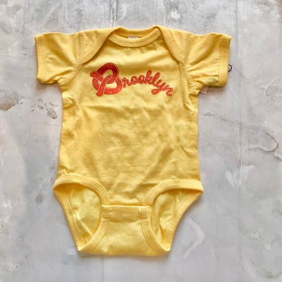 yellow cotton baby onesie with Brooklyn written with the pretzel being the "B" 