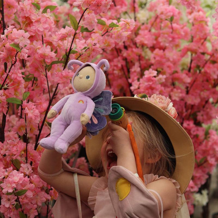 little girl holding up a dinky dinkum doll, this doll is dressed as a purple butterfly. the doll looks small compared to the little girl.