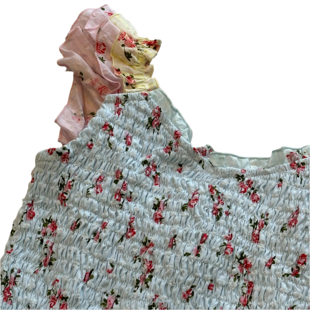 close up of the fabric with the tiny pink roses on it and blue base and the ruffle that is pink and yellow . 