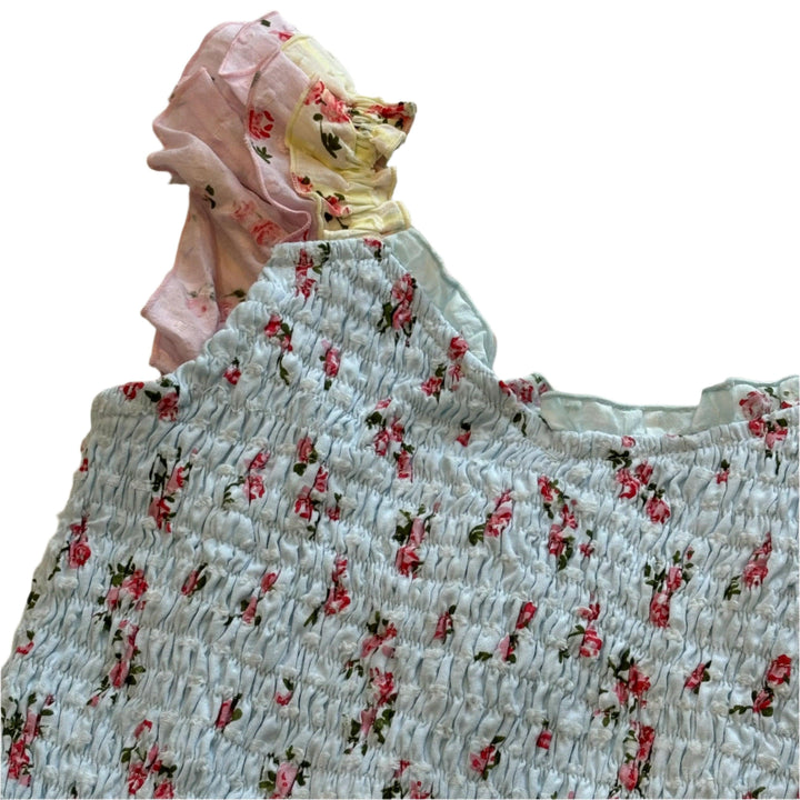 close up of the fabric with the tiny pink roses on it and blue base and the ruffle that is pink and yellow . 