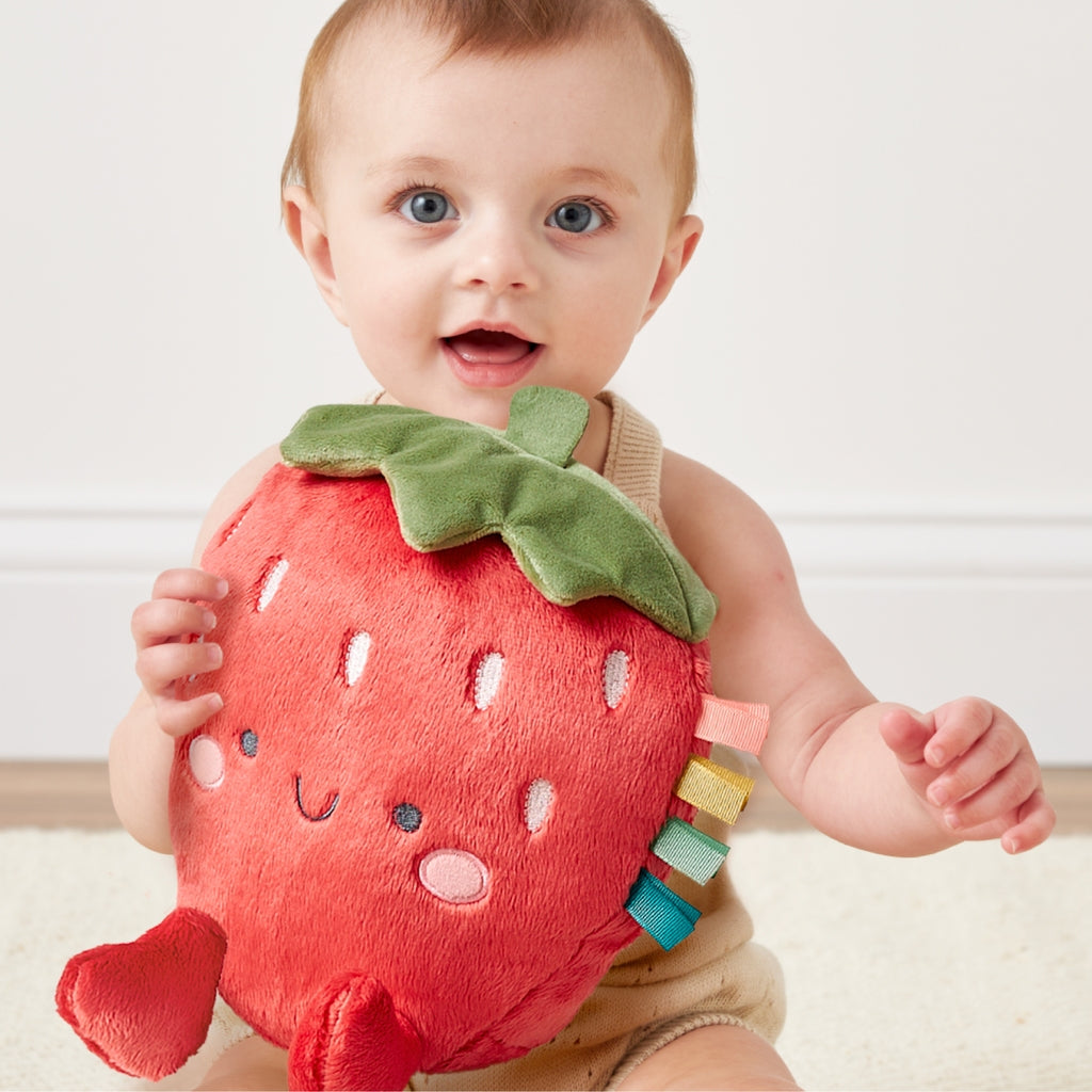 Baby holding a plush strawberry toy against a plain background