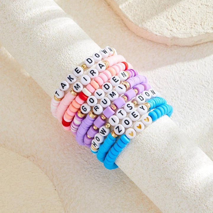 Set of colorful beaded bracelets with letter beads on a beige surface
