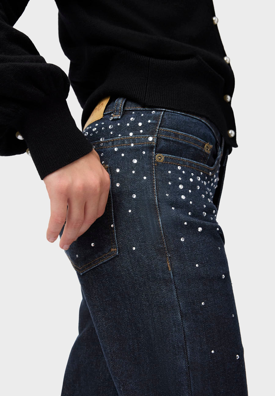Dark blue jeans with silver studs worn by a person on a light gray background