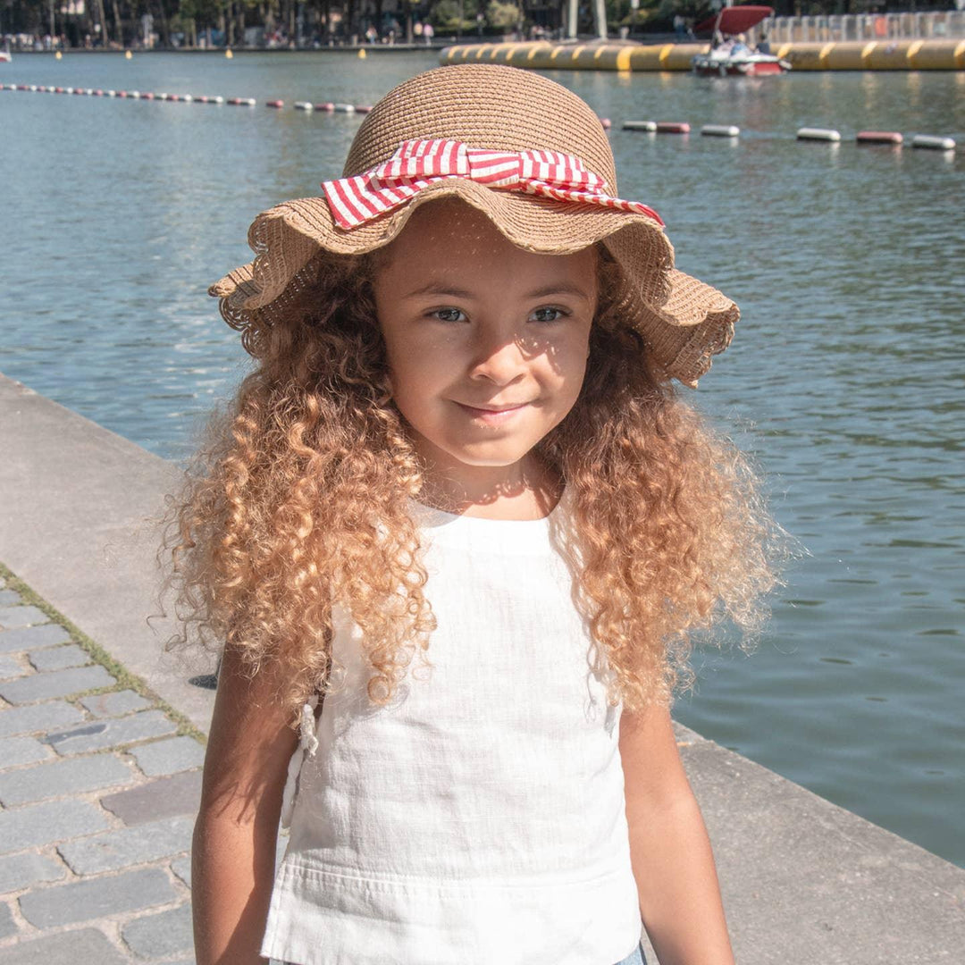 little girl modeling the straw hat with with red and white ribbon on the hat. 