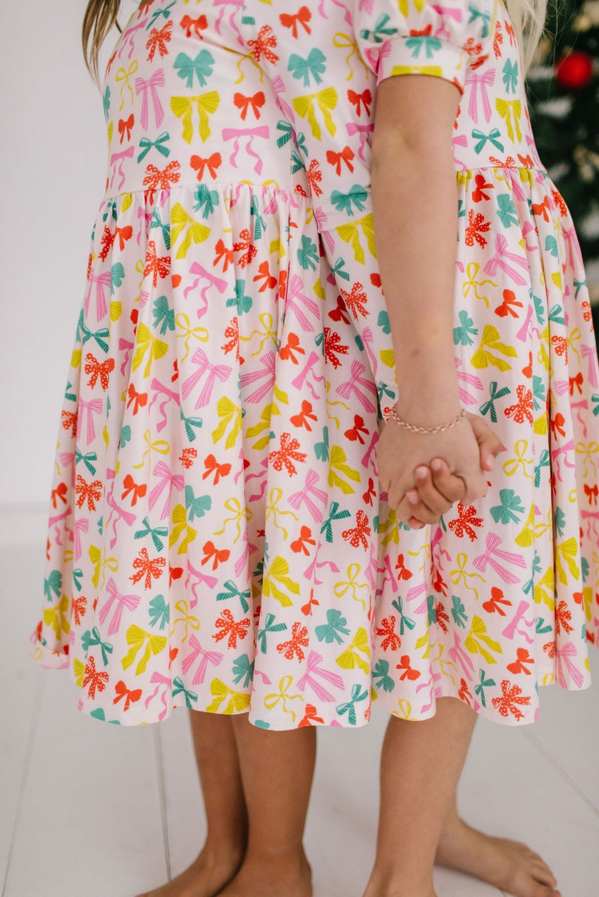 Child wearing a colorful dress with bow pattern on a white background