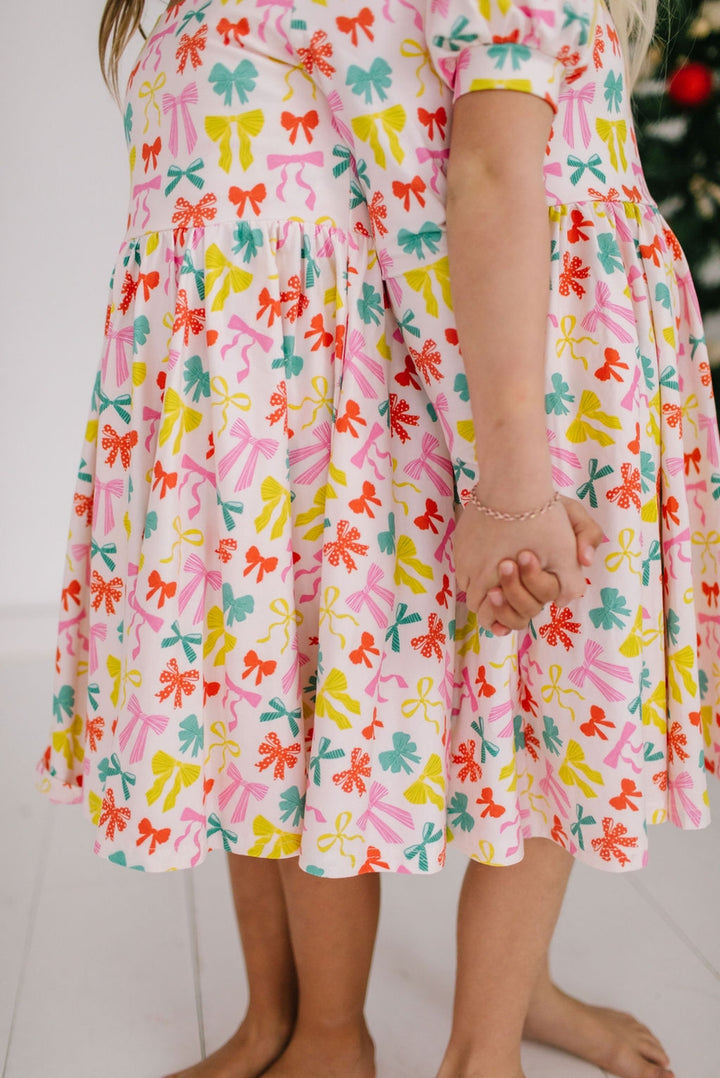 Child wearing a colorful dress with bow pattern on a white background